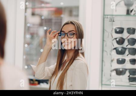 Primo piano di una splendida giovane donna sorridente che raccoglie e sceglie i bicchieri all'angolo ottico del centro commerciale. Felice Foto Stock