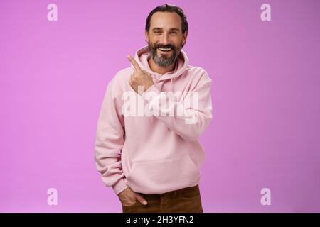 Affascinante amichevole felice uomo maturo 50s ported capelli grigi ridendo felicemente puntando angolo superiore sinistro dietro mostrando orgogliosamente fami Foto Stock