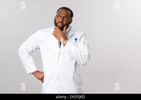 Covid19, concetto di assistenza sanitaria e clinica. Medico maschile afroamericano pensando ai sintomi del paziente, guardare via serio, ponderi Foto Stock