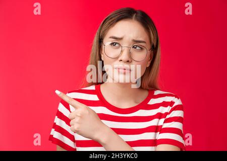 Deluso dubbia accigliata ragazza asiatica che fa domanda rassicurare, guardando a sinistra che punta dispiaciuto, non impressionato con strano p Foto Stock