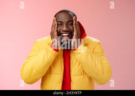 Felice carismatico giocoso afroamericano barbuto ragazzo in giallo giacca rosso felpa con cappuccio palmi guance sorridere amichevole Foto Stock