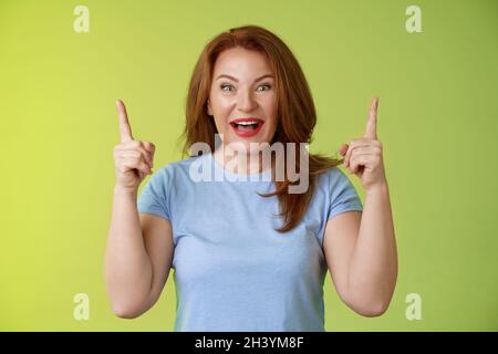 Impressionato entusiasta felice allegro di mezza età matura donna capelli rossi sorridenti stupito sguardo ammirazione gioia che punta su sollevare Foto Stock