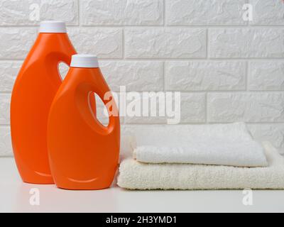 Due bottiglie di plastica arancione di detergente liquido e una pila di asciugamani su uno scaffale bianco, lavaggio a casa Foto Stock