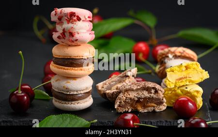 Pila di macaron multicolore e ciliegie rosse mature su sfondo di legno nero Foto Stock