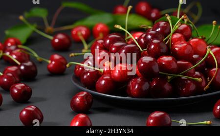 Ciliegie rosse mature in un piatto di ceramica su un tavolo di legno nero Foto Stock