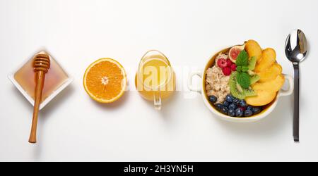 Piatto con farina d'avena e frutta, mezzo succo d'arancia maturo e spremuto di fresco in un decanter trasparente in vetro, miele in una ciotola sopra Foto Stock