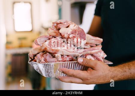 Una ciotola di costolette di agnello crude, affettate per grigliare, nelle mani maschili dello chef. Foto Stock