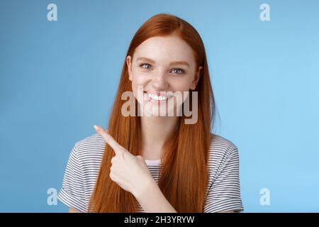 Primo piano attraente delicato tenero amichevole-guardare sorridente redhead donna mostra luogo che punta in alto a sinistra angolo indice dito grin Foto Stock