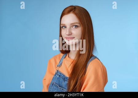 Vita-up tipo sincero tenero bella redhead ragazza indossa arancione camicia tute in denim in piedi mezzo-girato sorridente silly delicato g Foto Stock