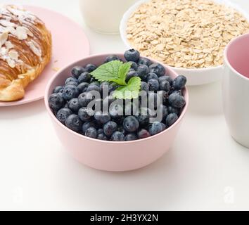 Mirtilli maturi in un piatto di ceramica rosa su un tavolo bianco, ingredienti per la colazione Foto Stock