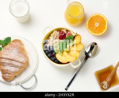 Piatto con farina d'avena e frutta, mezzo succo d'arancia maturo e spremuto di fresco in un decanter trasparente in vetro, miele in una ciotola sopra Foto Stock