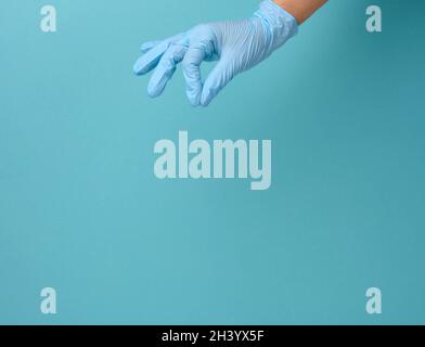 La mano del medico in un guanto medico blu tiene un oggetto su uno sfondo blu Foto Stock