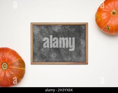 Telaio in gesso di legno vuoto e zucche arancioni mature rotonde su sfondo bianco, vista dall'alto Foto Stock