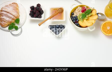 Piatto con farina d'avena e frutta, mezzo succo d'arancia maturo e spremuto di fresco in un decanter trasparente in vetro, miele in una ciotola sopra Foto Stock