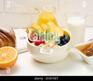 Piatto con farina d'avena e frutta, mezzo succo d'arancia maturo e spremuto di fresco in un decanter trasparente in vetro, miele in una ciotola sopra Foto Stock