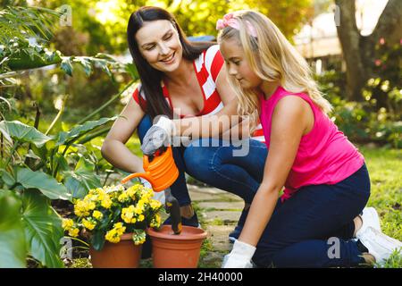 Sorridendo la madre caucasica e la figlia che lavorano in giardino indossando guanti e parlando Foto Stock