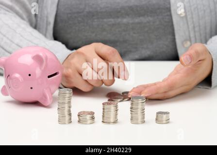 Pila di monete metalliche e una banca di porcellini rosa in ceramica. Uomo contando denaro, concetto di povertà, pianificazione del bilancio Foto Stock