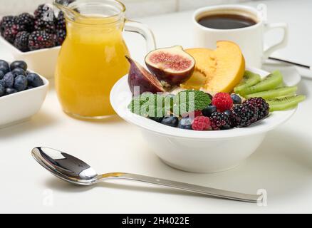 Piatto completo con farinata d'avena e frutta, succo appena spremuto in un decanter trasparente in vetro, tazza di caffè su un tavolo bianco. Healt Foto Stock