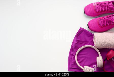 Un paio di sneaker sportive viola in tessuto, cuffie wireless, un asciugamano e una bottiglia d'acqua su sfondo bianco. Abbigliamento sportivo Foto Stock