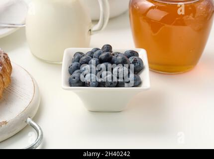 Mirtilli maturi in un piatto di ceramica bianca su un tavolo bianco, ingredienti per la colazione Foto Stock