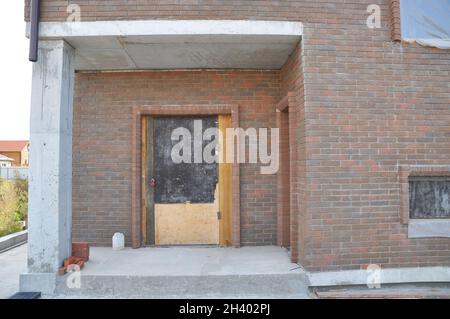 Proteggere la porta di ingresso e le finestre della casa incompiuta per l'inverno per evitare neve e pioggia all'interno. Foto Stock