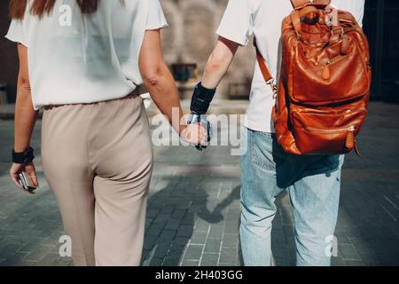 Giovane uomo disabile con mano protesica artificiale che cammina e tiene la mano della ragazza della donna. Foto Stock