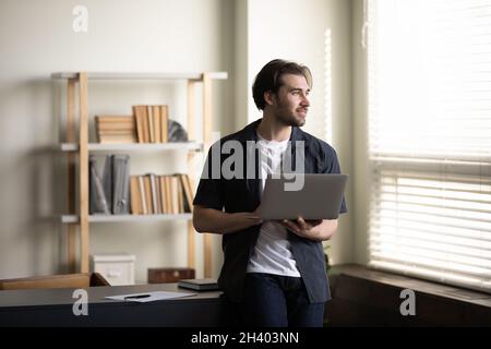 Sognante giovane uomo d'affari che tiene il computer nelle mani. Foto Stock