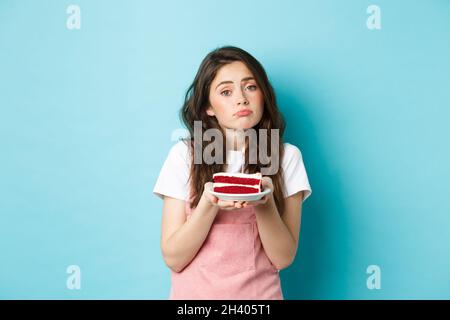 Vacanze e festeggiamenti. Ragazza triste carina guardando la macchina fotografica sconvolta, tenendo torta di compleanno con candela, sensazione di moody il b-giorno, stan Foto Stock