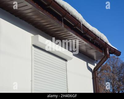 Gocciolatoio pieno di ghiaccio e neve in inverno. Ghiaccio congelato in una grondaia del tetto della casa, soffit di plastica e tapparelle per la protezione domestica. Foto Stock