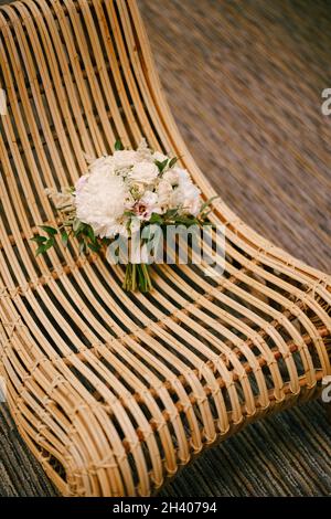 Bouquet nuziale di peonie bianche, rose, eustoma rosa, astilbe e rami di eucalipto su una sedia di paglia Foto Stock