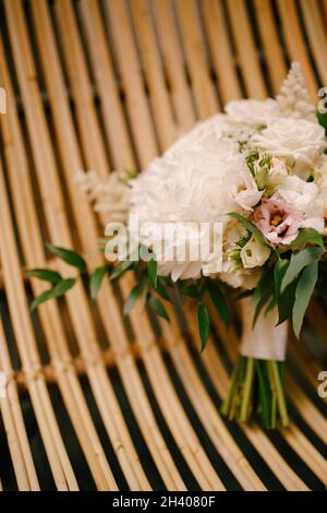 Bouquet nuziale di peonie bianche, rose, eustoma rosa, astilbe e rami di eucalipto su una sedia di paglia Foto Stock