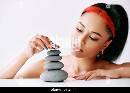 Graziosa donna afroamericana che fa la piramide delle pietre su sfondo bianco Foto Stock