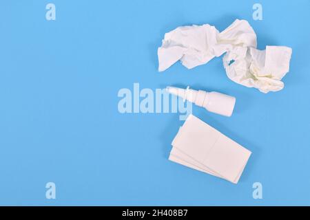 Vista dall'alto del flacone spray nasale e dei tessuti utilizzati durante il comune raffreddore su sfondo blu Foto Stock