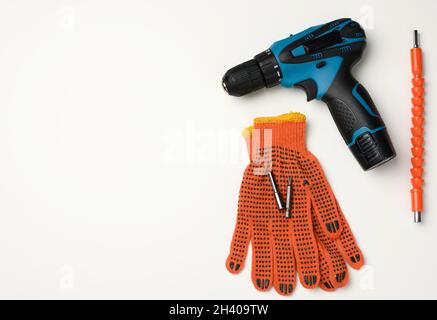 Un paio di guanti da lavoro in tessuto arancione e un trapano portatile su una batteria si trovano su un tavolo bianco Foto Stock