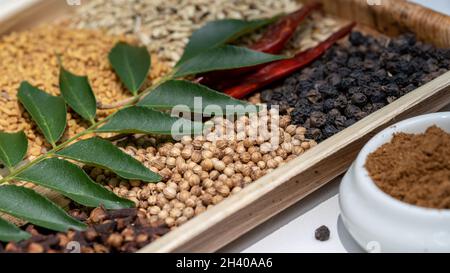 Ingredienti alimentari in cucina Pepe, coriandolo, finocchio, chiodi di garofano, fiocchi di finocchio, semi di cumino con foglia di curry in foglia di palma vista ravvicinata Foto Stock