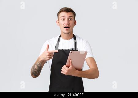 Concetto di piccola impresa, caffetteria e impiegati di cafe'. Bel cameriere o barista preoccupato in negozio che punta al tablet digitale, Foto Stock