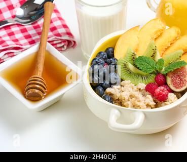 Piatto con farina d'avena e frutta, miele in una ciotola su un tavolo bianco Foto Stock