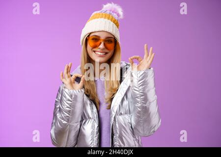 Tutto bene Grazie. Affascinante flirty bionda donna fiduciosa in argento elegante giacca occhiali da sole cappello invernale mostra okay nessun promble Foto Stock