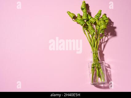 Vaso trasparente in vetro con fiori secchi verdi su un tavolo bianco, sfondo rosa Foto Stock