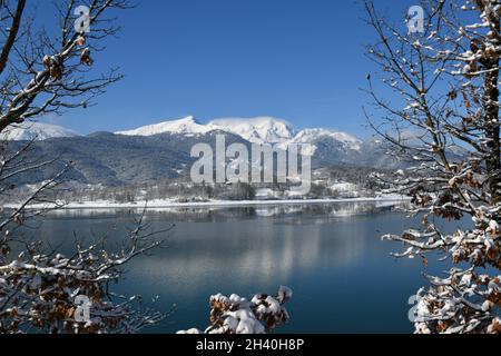 Lago innevato con foresta di abeti e montagne innevate sullo sfondo. Lago Plastiras. KARDITSA, Grecia centrale Foto Stock