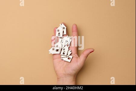 La mano della donna contiene case in legno in miniatura. Concetto di ricerca immobiliare per affitto, ipoteca, assicurazione immobiliare Foto Stock