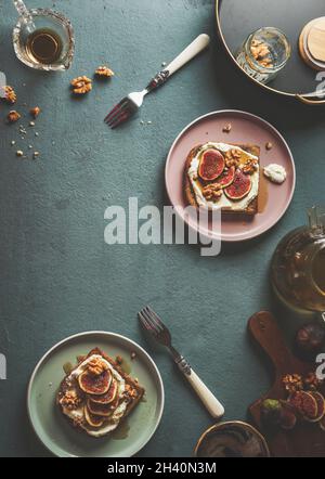 Gustosa prima colazione con toast alla francese con panna montata, fichi e noci affettati su tavolo da cucina in cemento con forchette e ciotole. Vista dall'alto con spazio di copia. Foto Stock