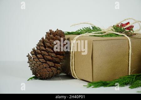 Confezione regalo Noel con cono di pino su sfondo bianco, foto dello spazio di copia da primo piano, messa a fuoco selettiva Foto Stock