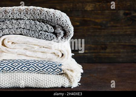 Accatastate coperte a maglia morbida contro uno sfondo rustico con messa a fuoco selettiva e sfondo sfocato. Spazio per fotocopie. Foto Stock