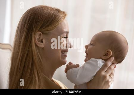 Vista del profilo sorridente giovane madre che ama giocare con il bambino Foto Stock