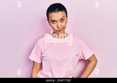 Bella donna ispanica con capelli corti indossando casual t shirt rosa scettico e nervoso, accigliato sconvolto a causa del problema. Persona negativa. Foto Stock