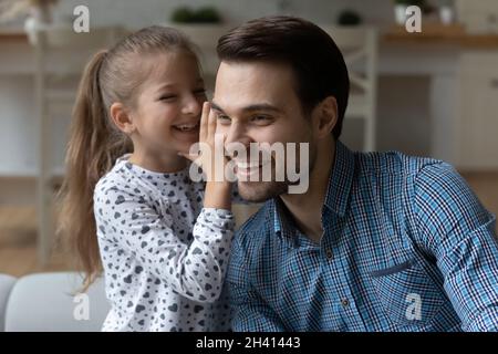 Piccola ragazza carina bambino felice che dice segreto a papà. Foto Stock