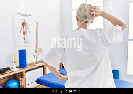 Giovane donna caucasica che lavora alla clinica di recupero del dolore all'indietro pensando al dubbio con mano sulla testa Foto Stock