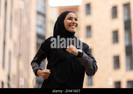 Stile di vita attivo. Giovane donna musulmana felice in modesto Sportswear jogging all'aperto Foto Stock