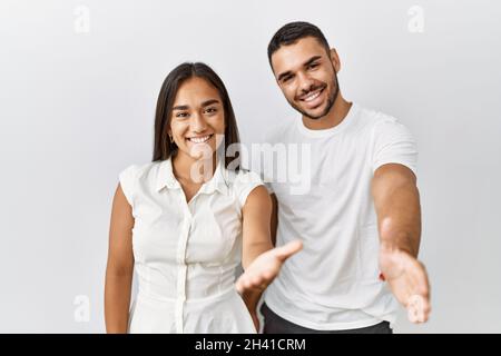 Giovane coppia interrazziale in piedi insieme in amore su sfondo isolato sorridente amichevole offrendo handshake come saluto e accogliente. Riuscito Foto Stock